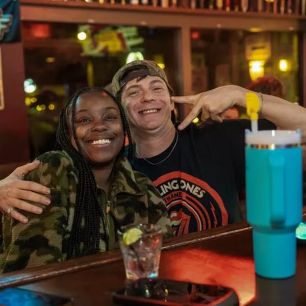 Smiling couple at Woody's bar, with drinks on the counter, enjoying the sports-bar atmosphere.