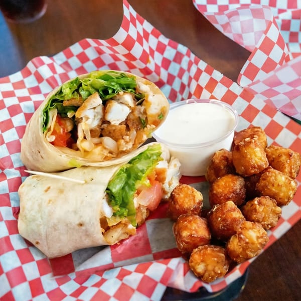 Two chicken wraps with lettuce and tomato, tater tots, and a side of ranch dressing.