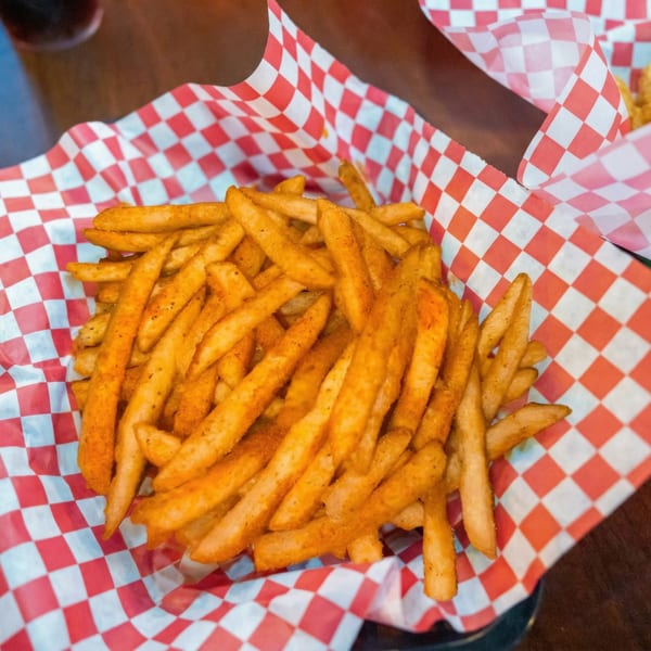 A basket of seasoned french fries in red and white checkered paper from Woody's @ City Market.