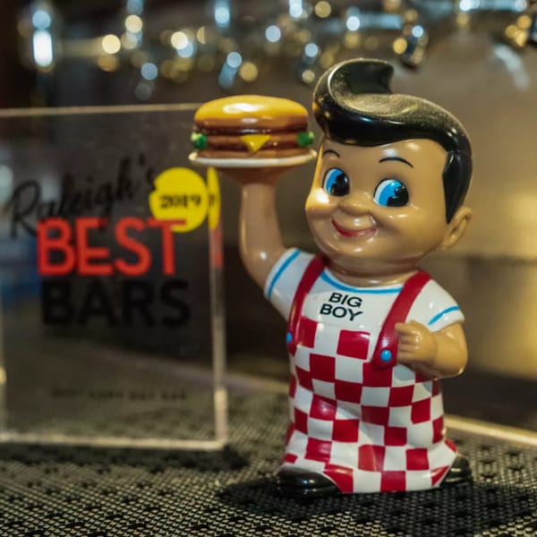 Big Boy statue holding a burger next to a "Raleigh's Best Bars 2019" award at Woody's.