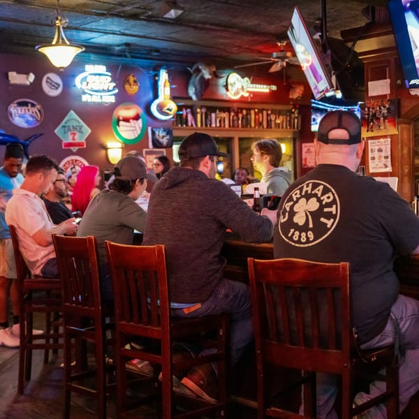 Patrons seated at a lively bar with neon signs and multiple TVs at Woody's @ City Market.