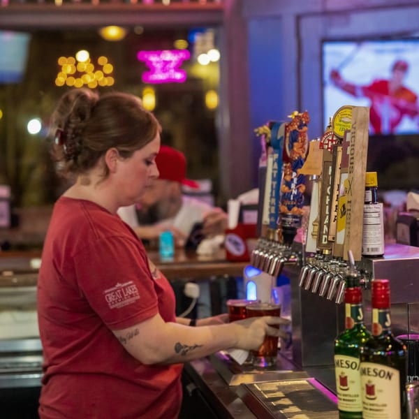A bartender in a red shirt pours a drink from a tap at Woody's @ City Market.