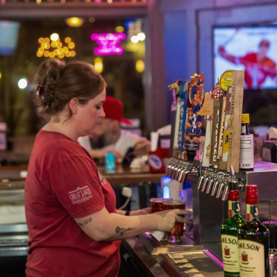 A bartender in a red shirt pours a drink from a tap at Woody's @ City Market.