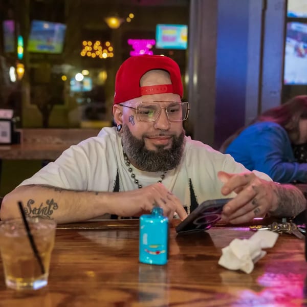 Man in red hat and glasses looking at his phone at the Woody's @ City Market bar.