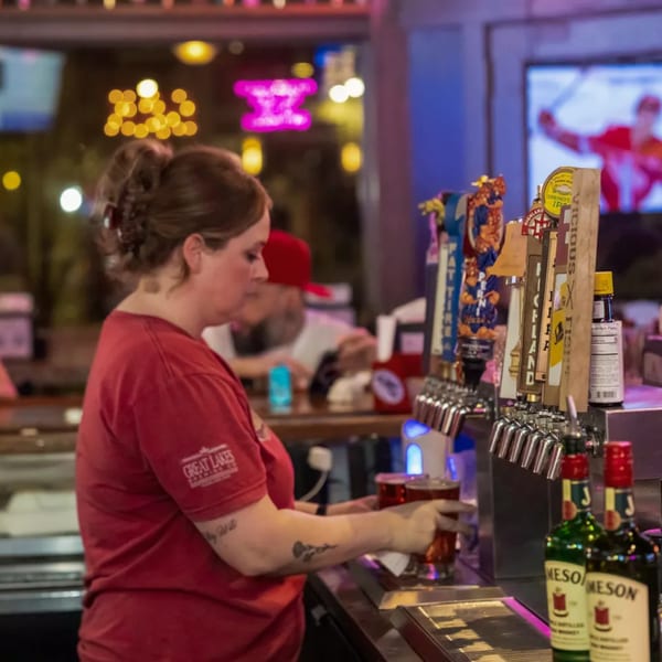 Bartender pouring a beer at Woody's @ City Market, with beer taps and Jameson bottles in the foreground.