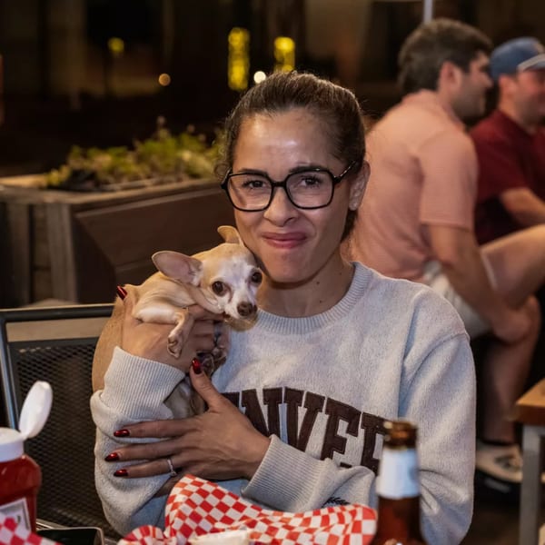 A woman in glasses smiles, holding a small dog at Woody's @ City Market.