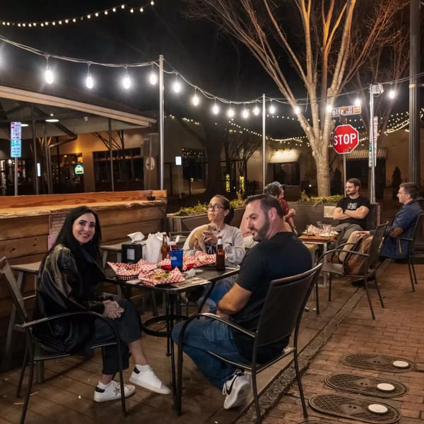 Patrons enjoying food and drinks on the outdoor patio of Woody's @ City Market at night.