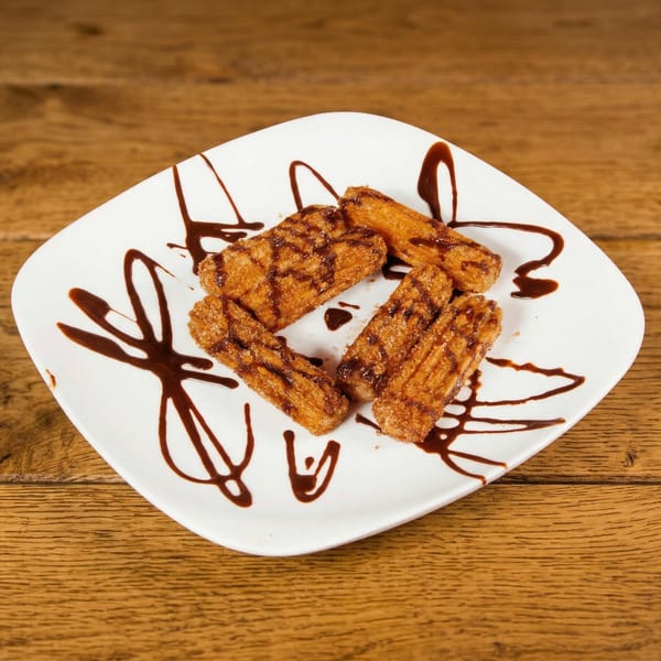 Four churro sticks drizzled with chocolate sauce on a white plate at Woody's @ City Market.