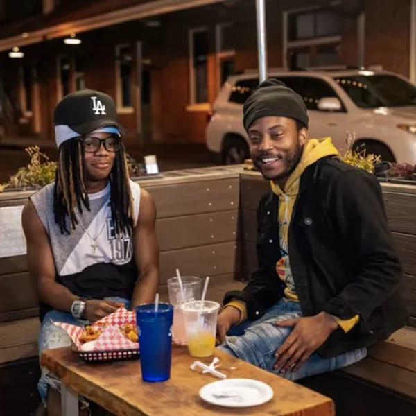 Two men enjoying drinks and a basket of fries at an outdoor table at Woody's.