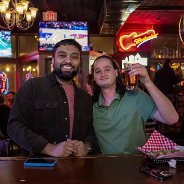 Two men smiling at the camera, one holding a beer, at Woody's sports bar.