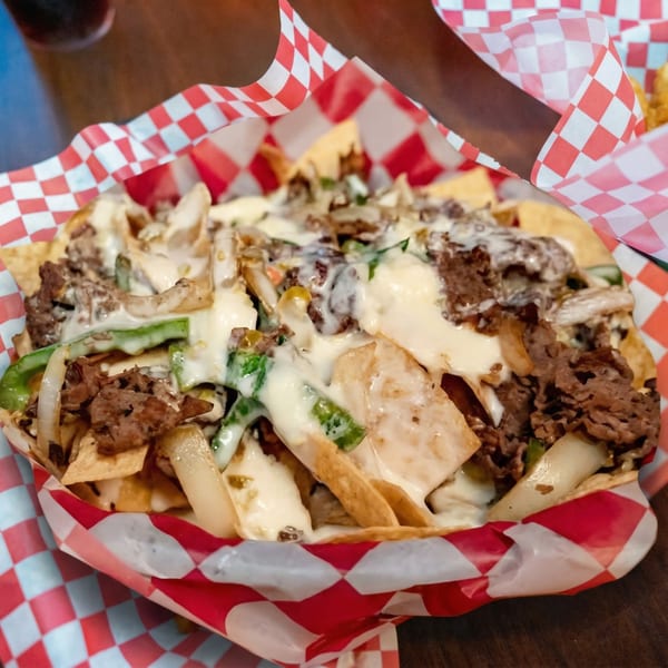 Cheesesteak nachos with steak, onions, peppers, and cheese sauce in a red and white checkered basket.
