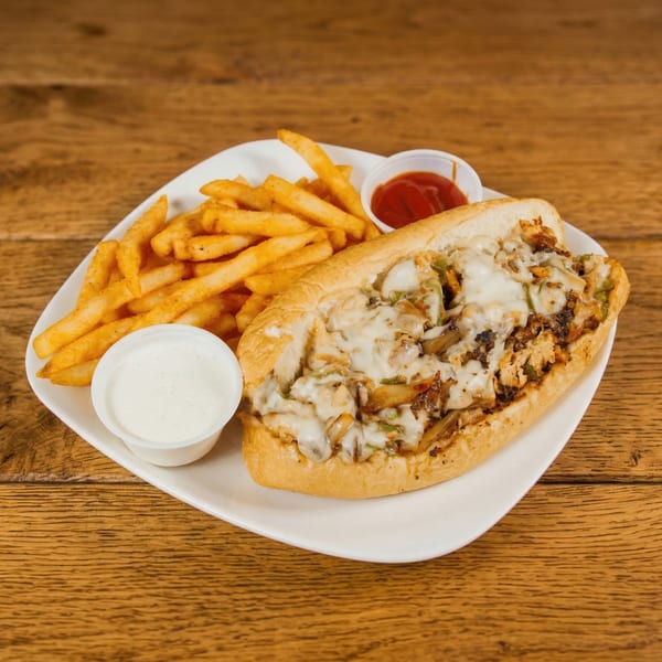 Cheesesteak sandwich with melted cheese, onions, and peppers, served with fries, ranch, and ketchup.